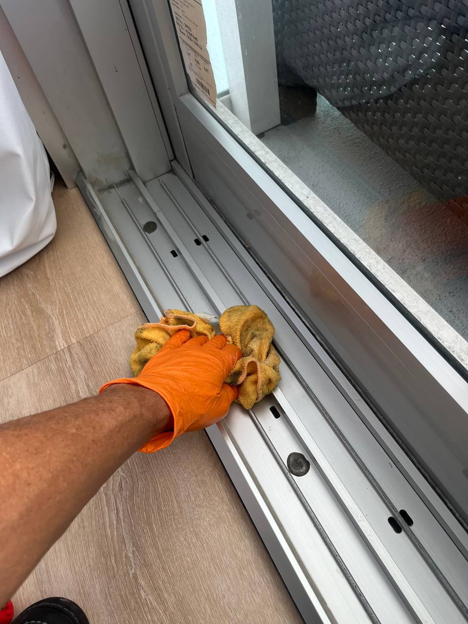 Technician wiping and sanitizing a sliding glass door track after treatment.