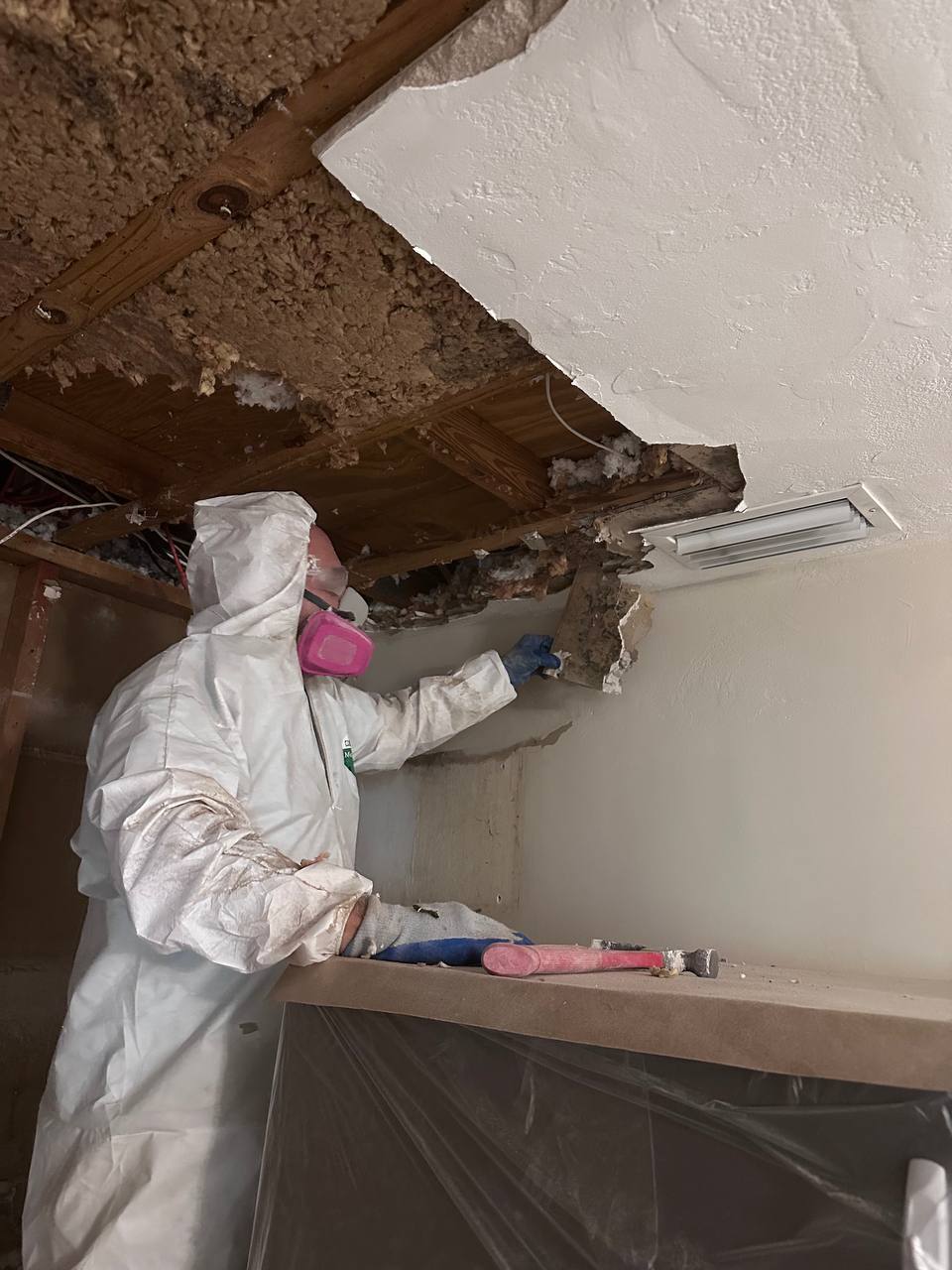 Technician removing moldy ceiling drywall near AC vent