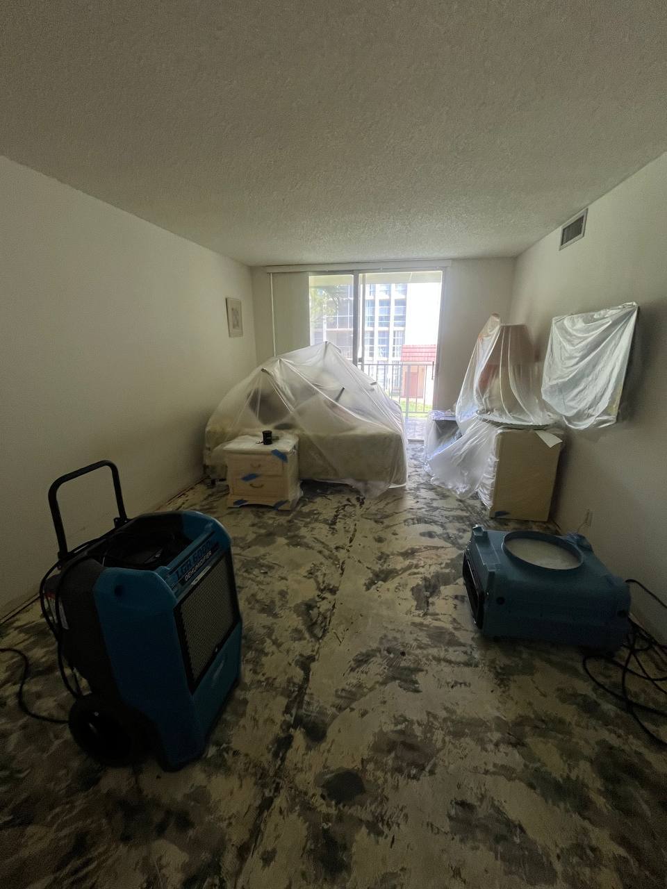 Commercial dehumidifiers and air movers deployed in room with plastic protection on furniture