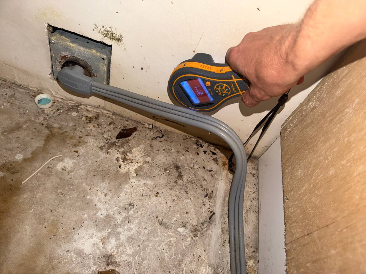 Moisture meter displaying high moisture reading near wall outlet during mold inspection