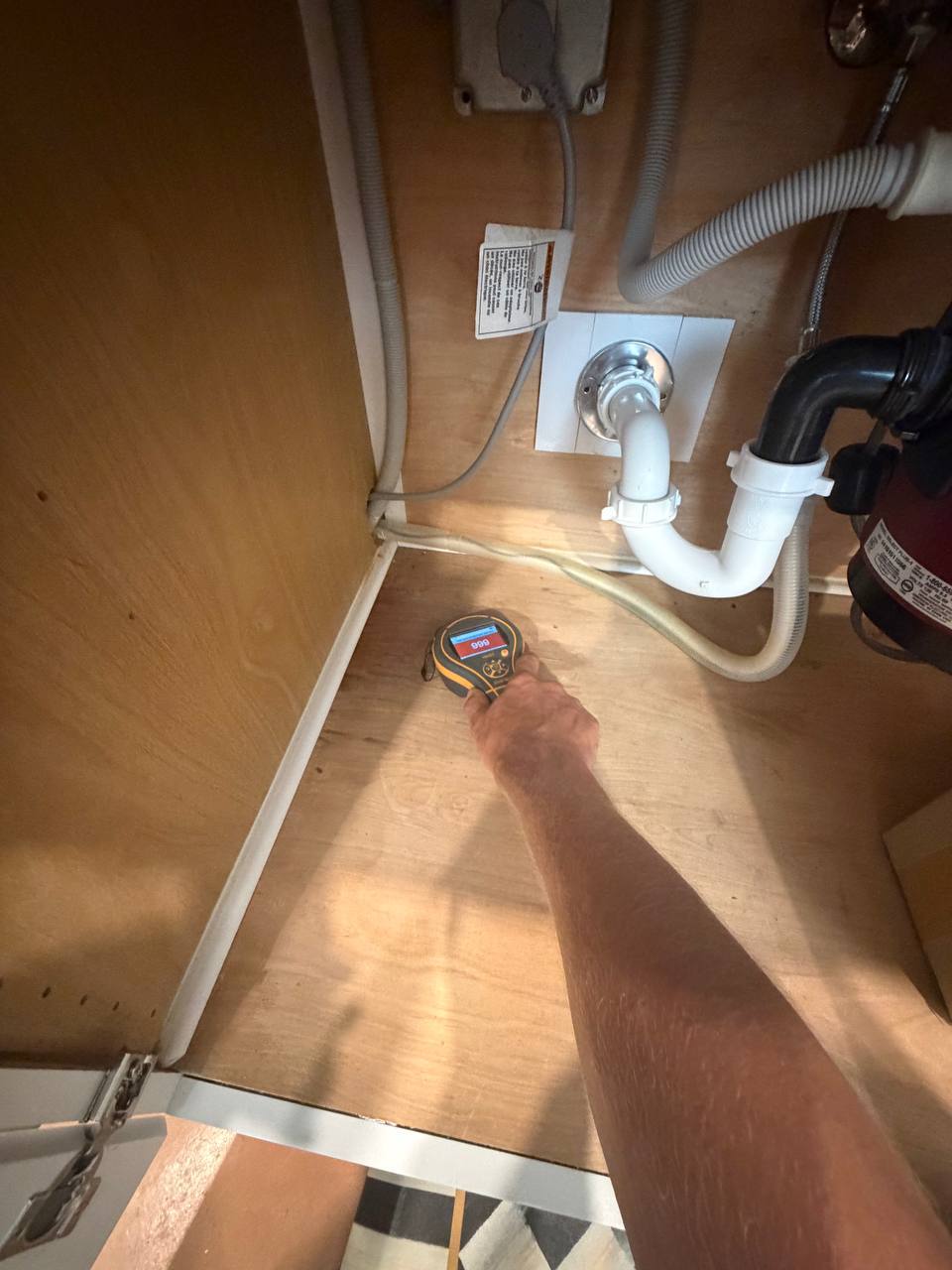 Moisture meter displaying maximum saturation level inside kitchen sink cabinet