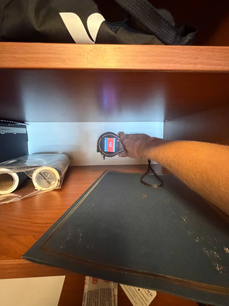Using moisture meter to test hidden wall saturation behind built-in closet unit