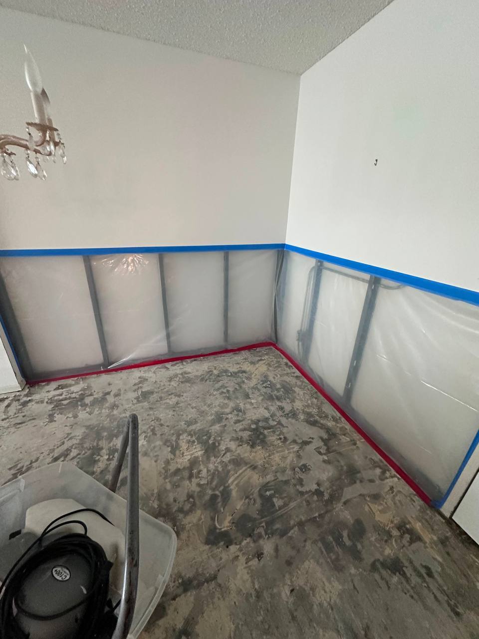 Lower drywall flood cut exposes metal framing covered with plastic containment sheetingApplying antimicrobial fogging treatment across remediated containment area