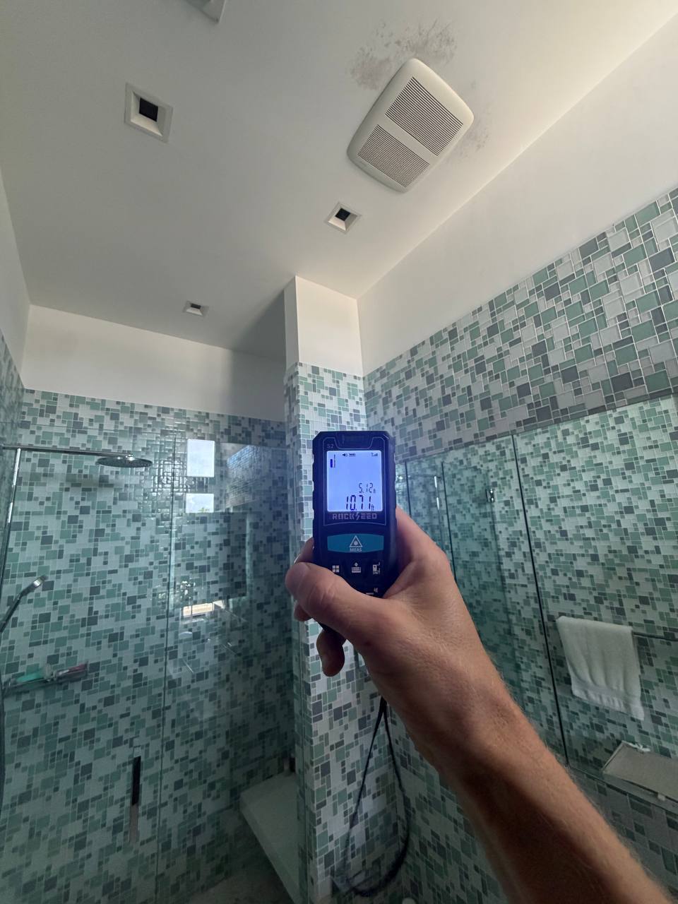 Measuring bathroom ceiling height and distance with a laser meter during mold assessment