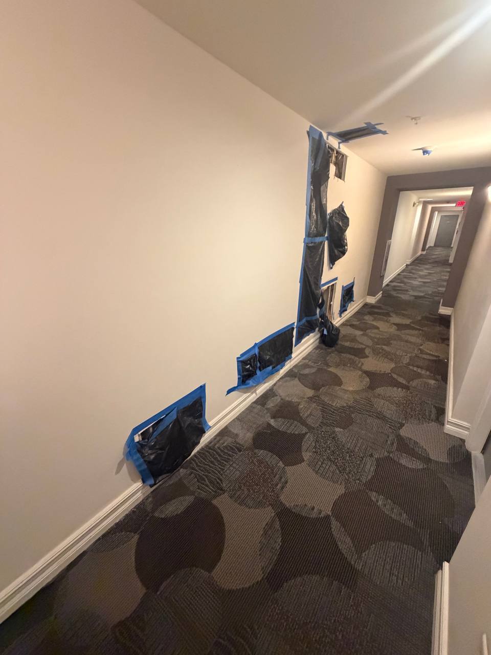 Hallway drywall cutouts and poly containment setup during water damage restoration
