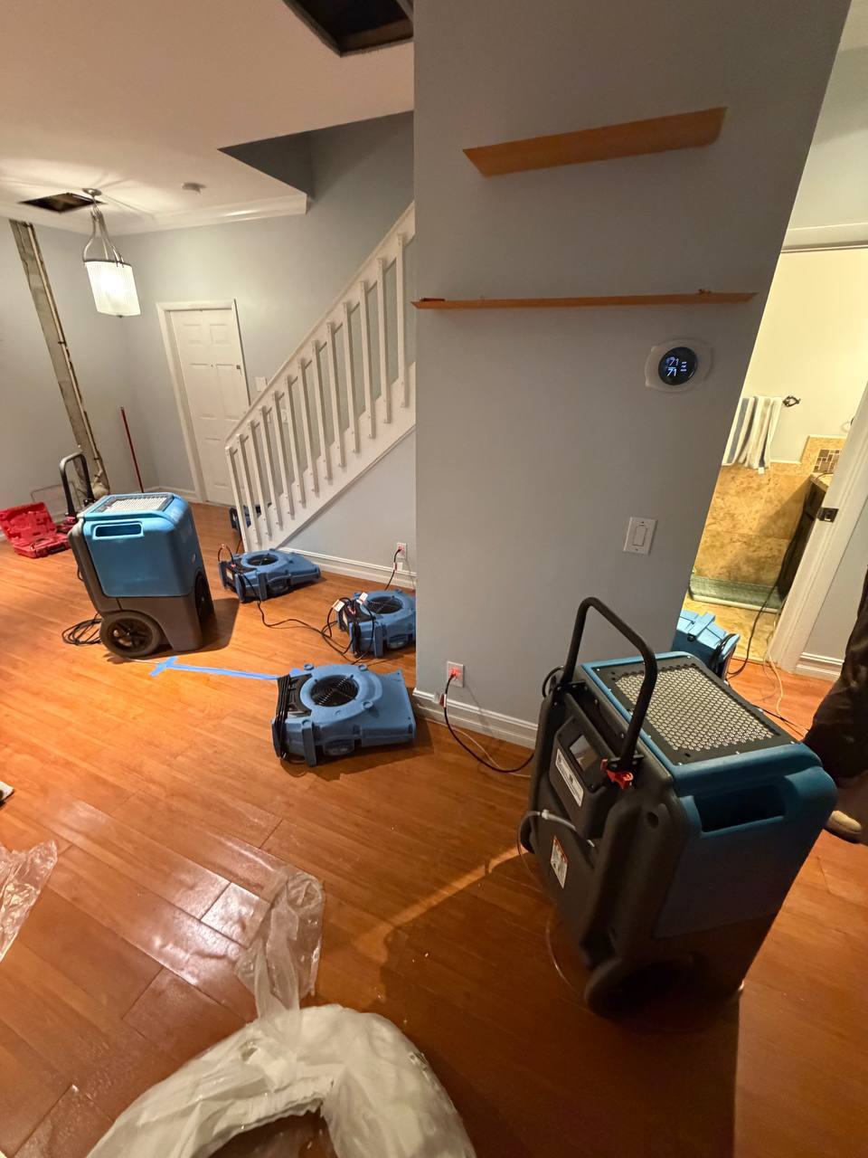 Structural drying equipment operating near staircase to dry saturated wood flooring
